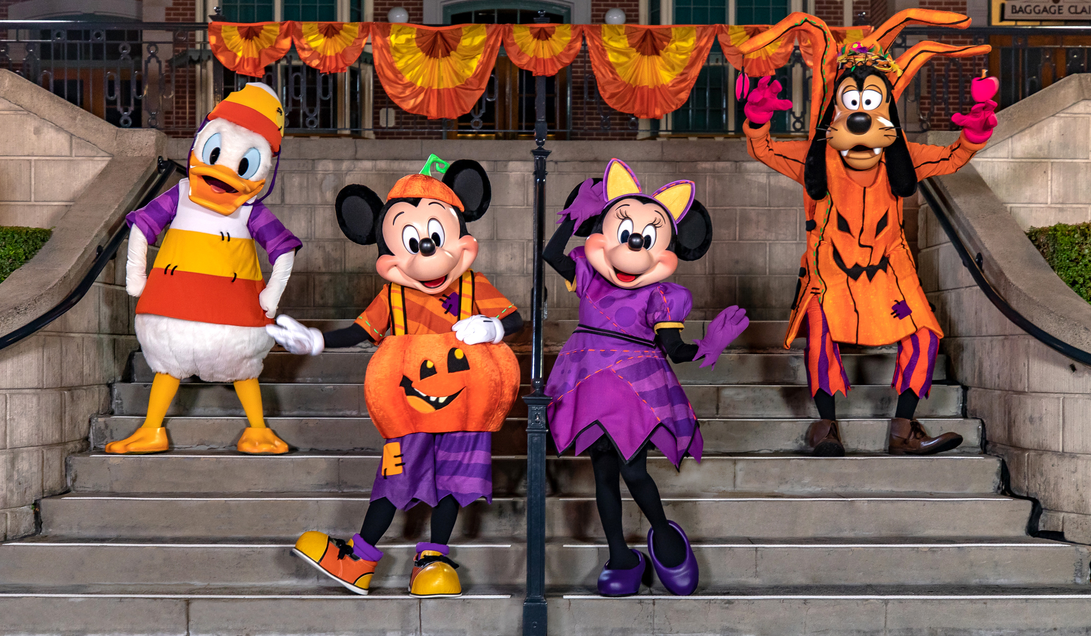 Donald, Mickey, Minnie and Goofy in Halloween costumes on the steps to the Main Street U.S.A. Train station at Disneyland.