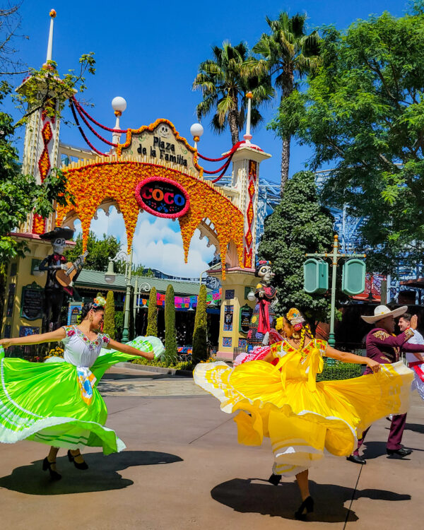 Dancers in bright yellow and green dresses for Dios De Los Muertos dancing in front of the Plaza de la Familia at Disney's California Adventure.