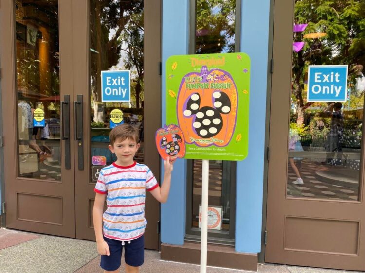 Sign for Pluto's Pumpkin Pursuit in Downtown Disney at Disneyland with child in front with a filled out card.