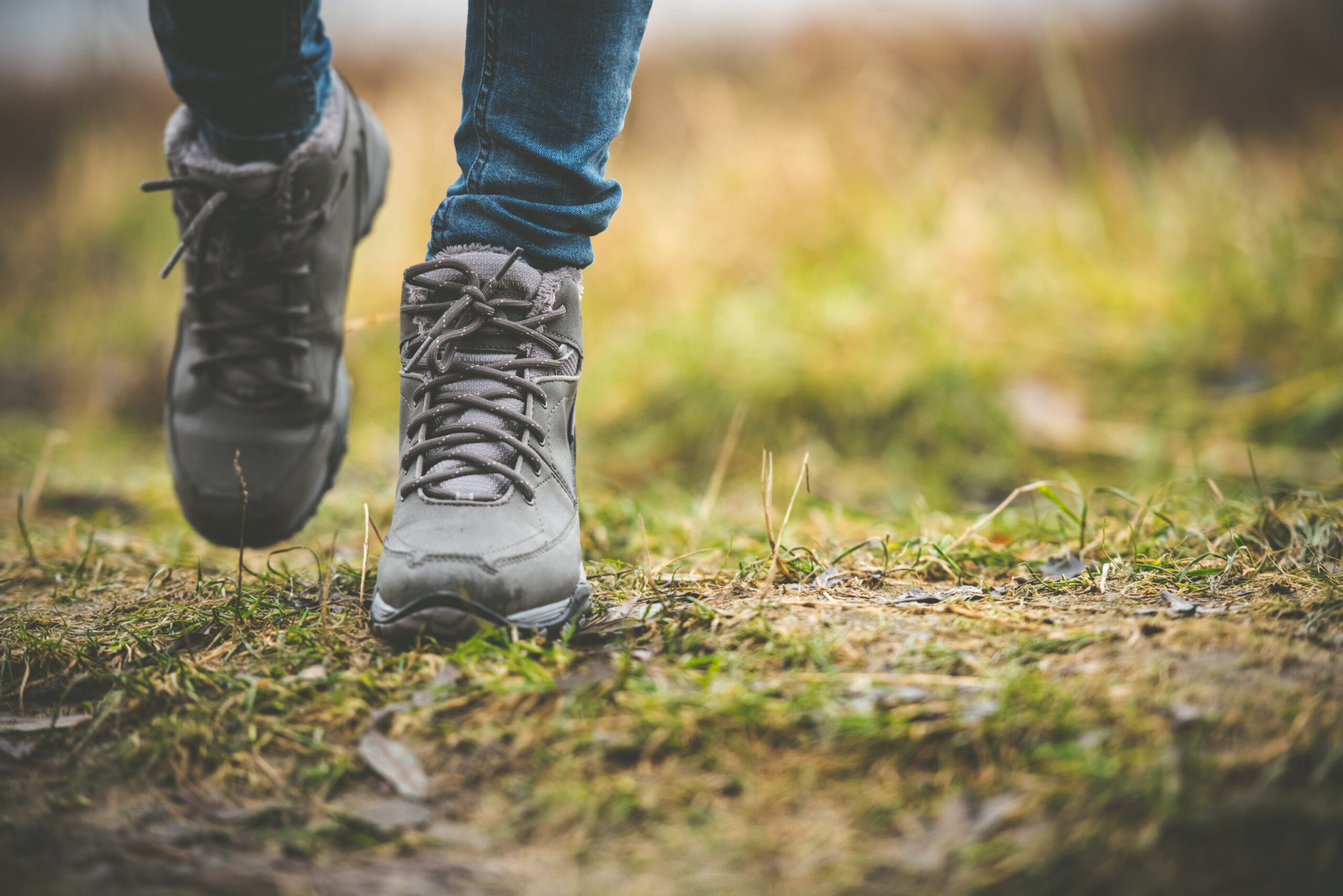 A close up of hiking boots on a person walking on a forest path.