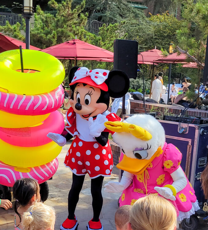 Minnie and Daisy next to a large stack of donut shaped pool floaties at a party by the Grand Californian Pools during summer at Disneyland