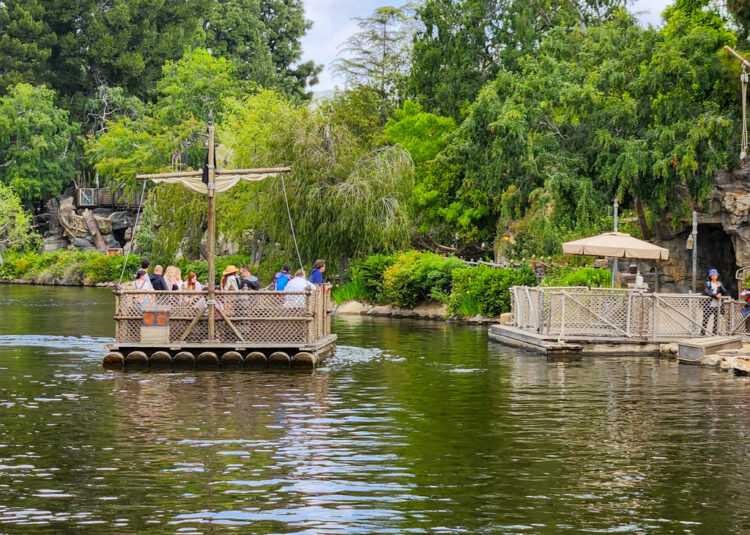 a raft on the rivers of America in Disneyland, filled with guests heading to the Pirates Lair on Tom Sawyer Island where kids can explore the trails and play areas.